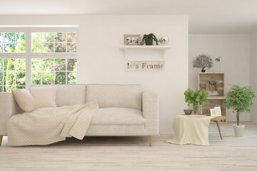 Obraz premium White living room with sofa and summer landscape in window. Scandinavian interior design. 3D illustration
