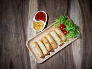 Fried spring rolls on a white plate and spicy sauce on wood table, top view.