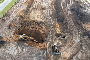The excavator digs a trench under the foundation, and the bulldozer clears the ground. Top view of a construction site