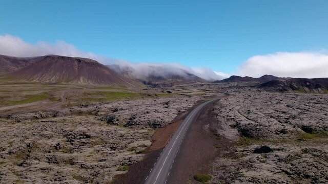 Aerial shot in Iceland over old lava fields, mountains with fog and mist. Road winds through the dramatic landscape.