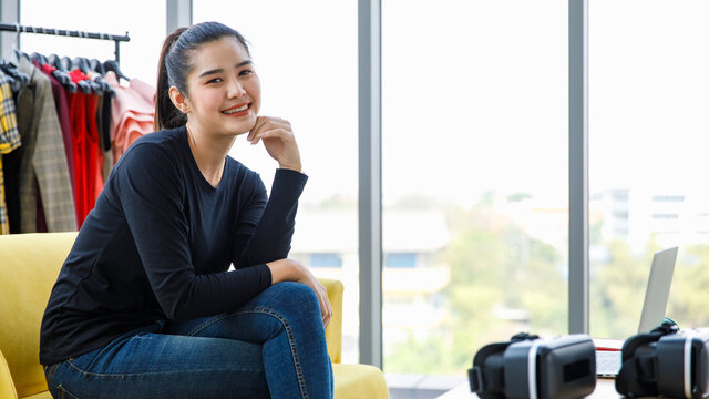 Asian young happy cheerful millennial successful female blogger vlogger businesswoman influenzer in casual outfit sit smiling laughing in home studio store selling clothes online via laptop computer