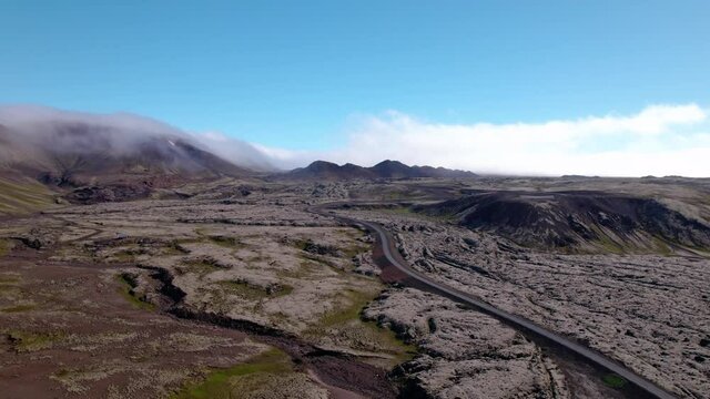 Aerial flying towards mountains in barren volcano landscape in Iceland. Single house below and fog surrounds mountains.