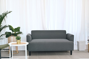 Comfortable sofa, white table and houseplants in bright living room interior.