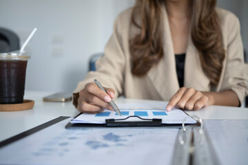 Fototapeta na wymiar Businesswoman holding pen and analyzing financial graph at office desk.
