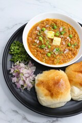 Indian Mumbai Street style Pav Bhaji, garnished with peas, raw onions, coriander, and Butter. Spicy thick curry made of out mixed vegetables served with pav over white background with copy space.
