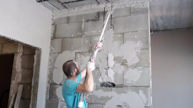 Plasterer Painter Applies a Layer of Liquid Plaster to Stone Wall with Spray Gun. Automatic Supply of Putty Mortar. Simplification of Builder's Manual Labor. Fast Plastering of Any Walls. Construction
