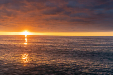 Bright orange sunset over the sea. Reflection by glare of sunlight in the water. Beautiful cloudy sky