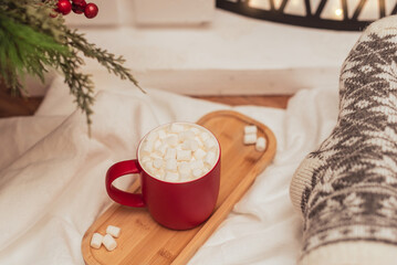 Obraz na płótnie Canvas Cozy vibes scene with a cup of hot drink with white marshmallows and female feet in warm woollen socks in front of fireplace. Selective focus. Cozy atmosphere during winter holidays concept