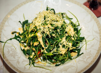 Portioned vegetable salad with arugula and grated parmesan cheese on a plate, close-up. Lunch at european restaurant.