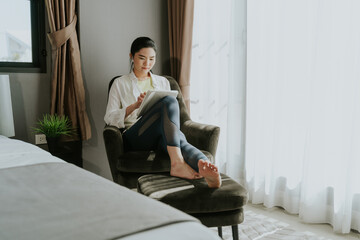 A young Asian woman in easy casual wear using digital tablet listening to music relaxing at home in the weekend