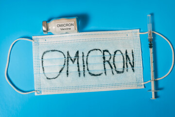 On a blue background lies a medical mask labeled Omicron, a syringe and a vial of vaccine. The...