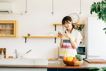 キッチンでスマホを持つ女性（スマホ・笑顔）
