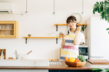 キッチンでスマホを持つ女性（スマホ・ガッツポーズ）
