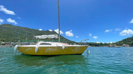 Naklejka na ściany i meble Yellow recreational sailing boat on ocean with mountain, blue sky and clouds in Hong Kong