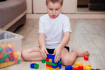 Boy in a white T-shirt playing with lots of colorful plastic blocks constructor