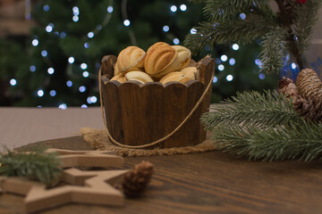 Nut-shaped cookies in a wooden cup on a wooden surface. In the background there are fir branches with cones.