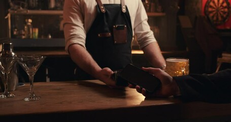 Caucasian bartender holding card machine while customer pays with cellular device 