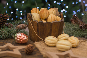 Nut-shaped cookies in a wooden cup on a wooden surface. In the background there are fir branches with cones.