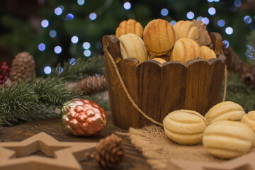 Nut-shaped cookies in a wooden cup on a wooden surface. In the background there are fir branches with cones.