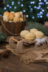 Nut-shaped cookies on a wooden sleigh. In the background there is a wooden cup with nuts, spruce branches with cones.