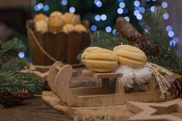 Nut-shaped cookies on a wooden sleigh. In the background there is a wooden cup with nuts, spruce branches with cones.
