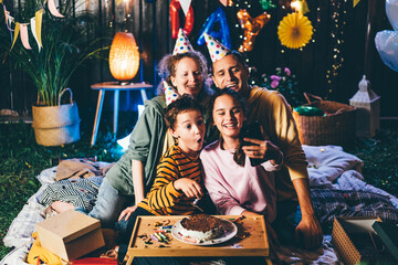 Pretty junior schoolgirl makes selfie with happy family in birthday cones with smartphone at...