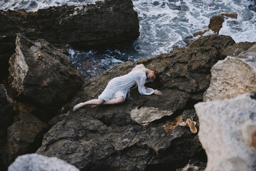 woman in long white dress wet hair lying on a rocky cliff unaltered