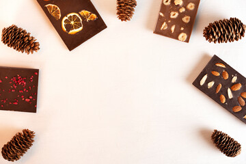 Natural organic milk and bitter chocolate bars with sublimated berries, orange slices, almond, hazelnut and fir cones. Copy space.