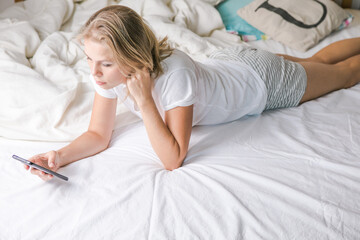 Obraz na płótnie Canvas Online dating. Romantic. Portrait of a smiling middle aged girl lying on bed with mobile phone. Happy blonde woman using cellphone at home. Beautiful young lady typing on smartphone in her bedroom.