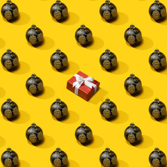 New Year's pattern from black christmas ball decoration with Gift box on yellow background. Christmas pattern made of New Year ball. Minimal Christmas or New Year concept.