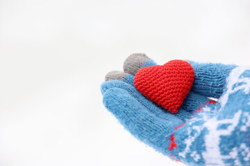 Red heart on palm of hand in warm knitted glove against the snow. Concept of a romantic love, Valentine's day or charity