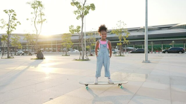 4K Portrait of Smiling little African child girl kid skateboarding at the park. Cute preschool girl enjoy and having fun outdoor lifestyle practicing extreme sport longboard skating on summer vacation