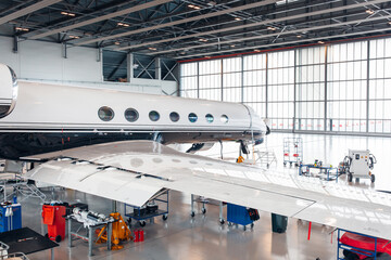 Maintenance of airplane in large white hangar - obrazy, fototapety, plakaty