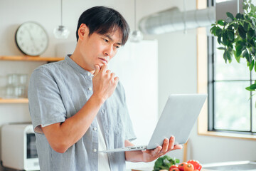 キッチンの前でパソコンを使う男性（困る）
