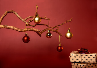 a long dry tree on which New Year's holiday balloons are hanging red and gold, and boxes with gifts for the holiday on a red background are lying at the bottom