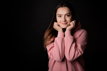 Cute young brunette in a pink hoodie, portrait on a black background.