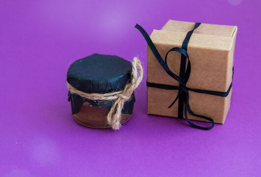 Gift Box Wrapped in Craft Paper with Black Ribbon and Small Glass Jar of Jam Healthy Product, Natural. Horizontally Copy space Close-up Handmade Vintage Present