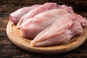 Raw chicken fillets on wooden board on dark wooden background.