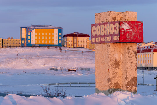 Anadyr, Chukotka, Russia - January 23, 2020. A sign near the road with the text in Russian "State farm named after the XXII Congress of the Communist Party of the Soviet Union" and colorful buildings.