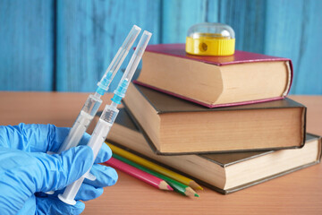 bottles and syringes of vaccine aganist covid-19 near book pile and school supplies, children...
