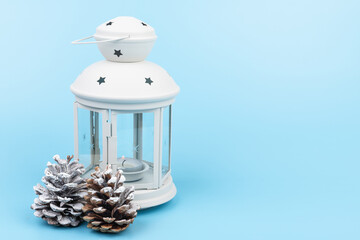 White lantern with candle inside and Christmas decoration on blue background. Copy space.