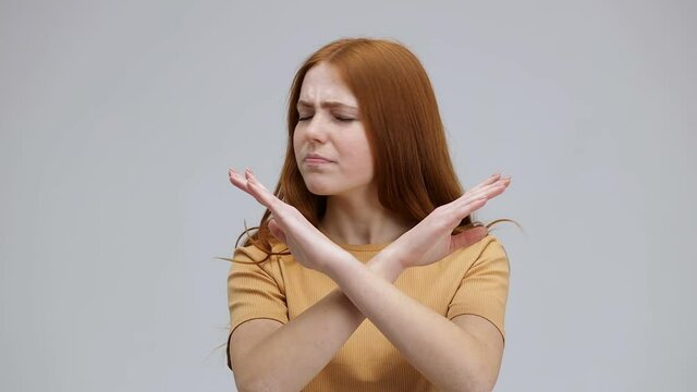 beautiful young woman saying NO to something denying, rejecting and making a gesture with her hands, standing isolated on gray background in studio. Negative reaction
