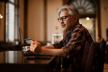 Man using laptop while sitting in cafe. Senior man holding credit card.