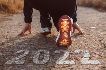 Fototapeta Text 2022 written on the road in the middle of asphalt road and athlete woman runner female feet in sneakers at the start for new year obraz