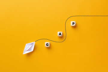 Origami paper boat passes through the wooden cube barriers with the word gap. Gap analysis in...