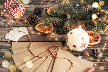 Christmas composition greeting letters in craft envelopes fir-tree branch and burning candle on a dark wooden background with bokeh