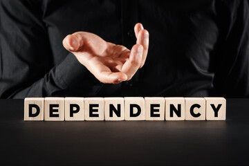 Male hand shows the wooden cubes with the word dependency