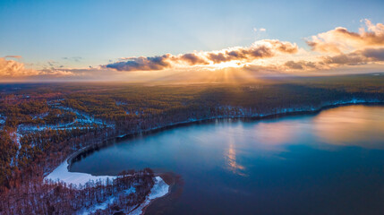 Aerial view of the winter background with a snow-covered forest, lake and sunrays over the Glukas lake in Lithuania