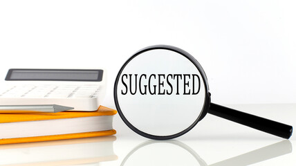 Magnifier with text SUGGESTED with notebook, calculator on the white background