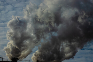 White and gray smoke and steam from a high concrete chimney against the bright blue sky